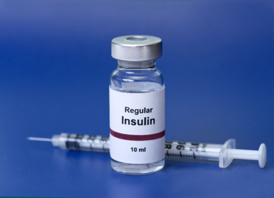 Regular insulin with insulin syringe on blue background. Label is not real.